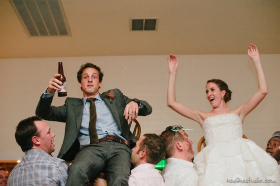 bride and groom lifted up in a chair, groom looking shocked
